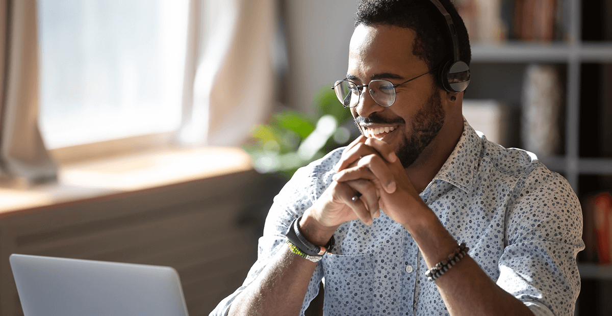 Student wearing glasses and an audio headset looking at their laptop and smiling.